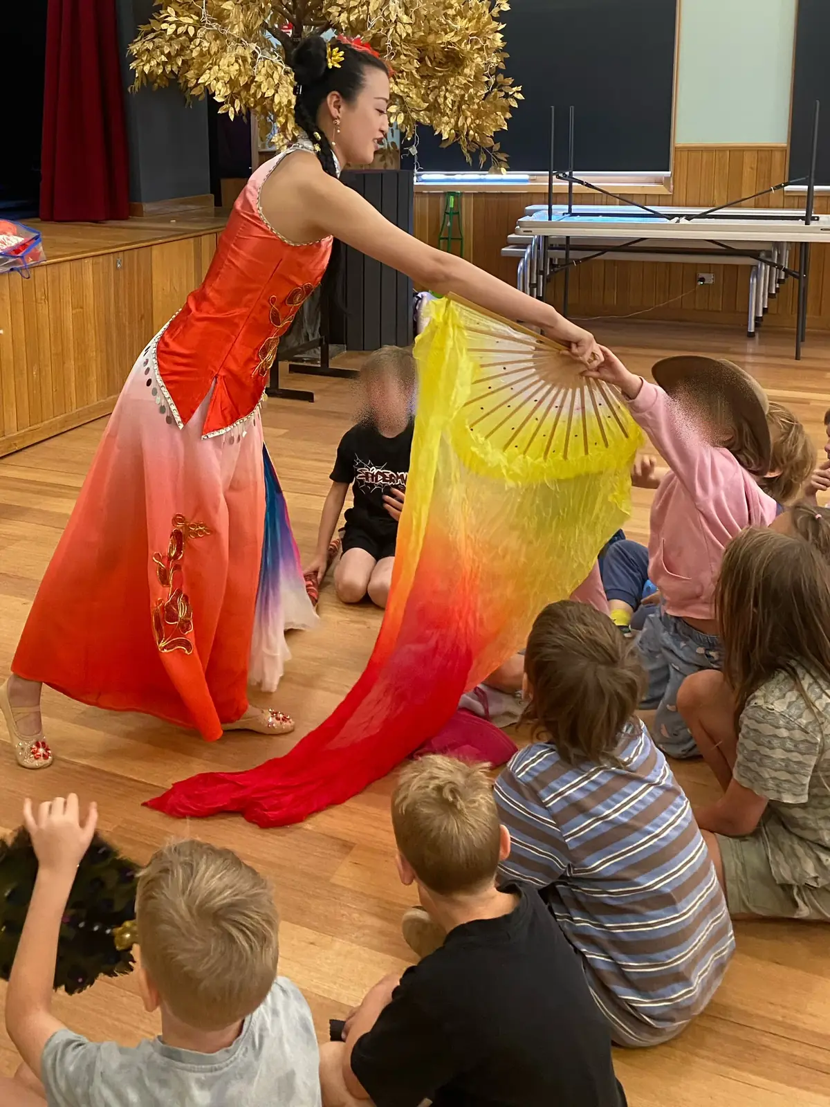 Raina sharing a long silk fan with seated children