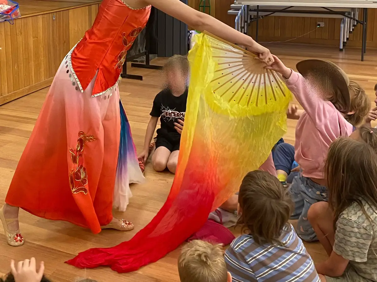 Raina sharing a long silk fan with seated children