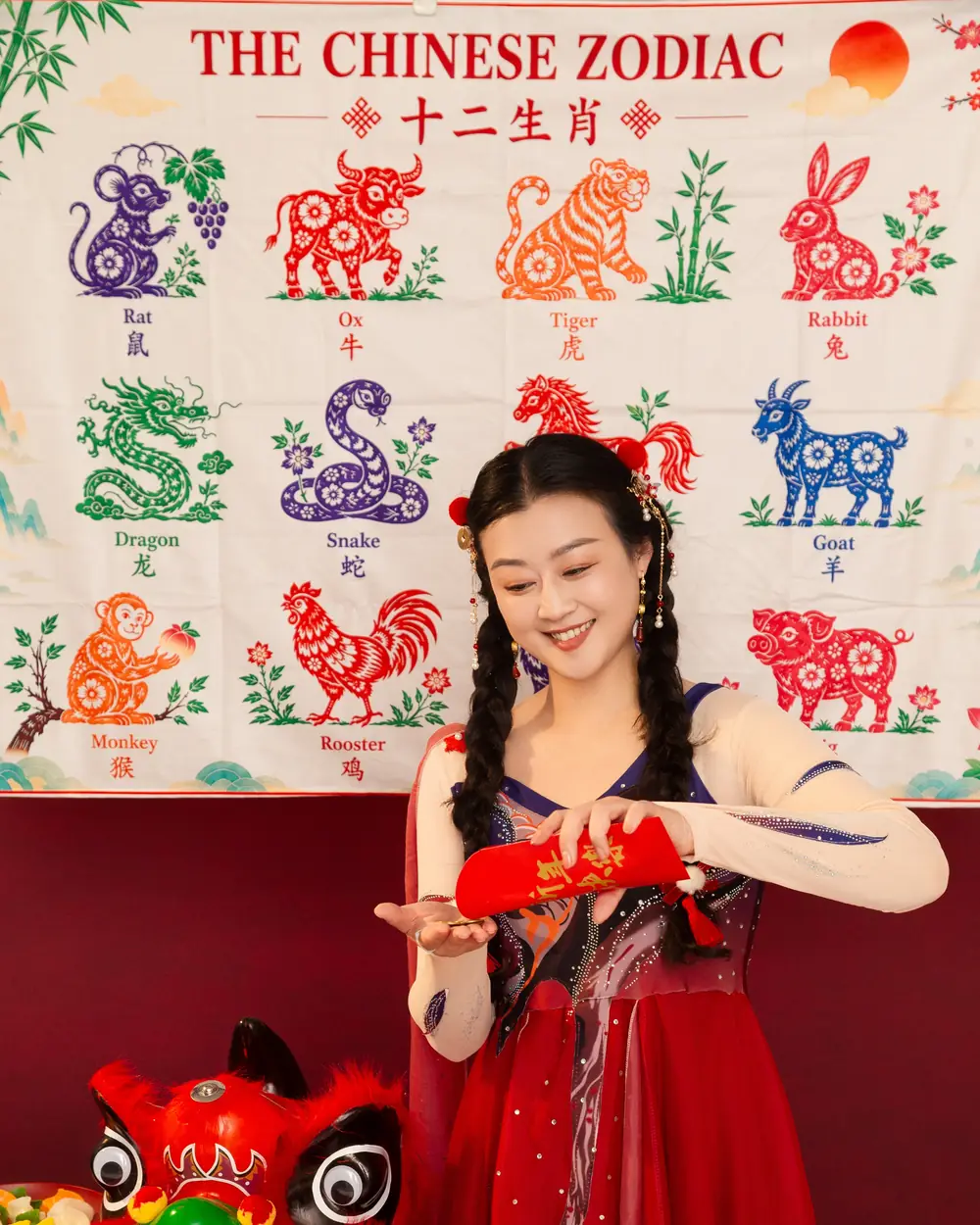Raina showing a red festive decoration beside a lion dance head