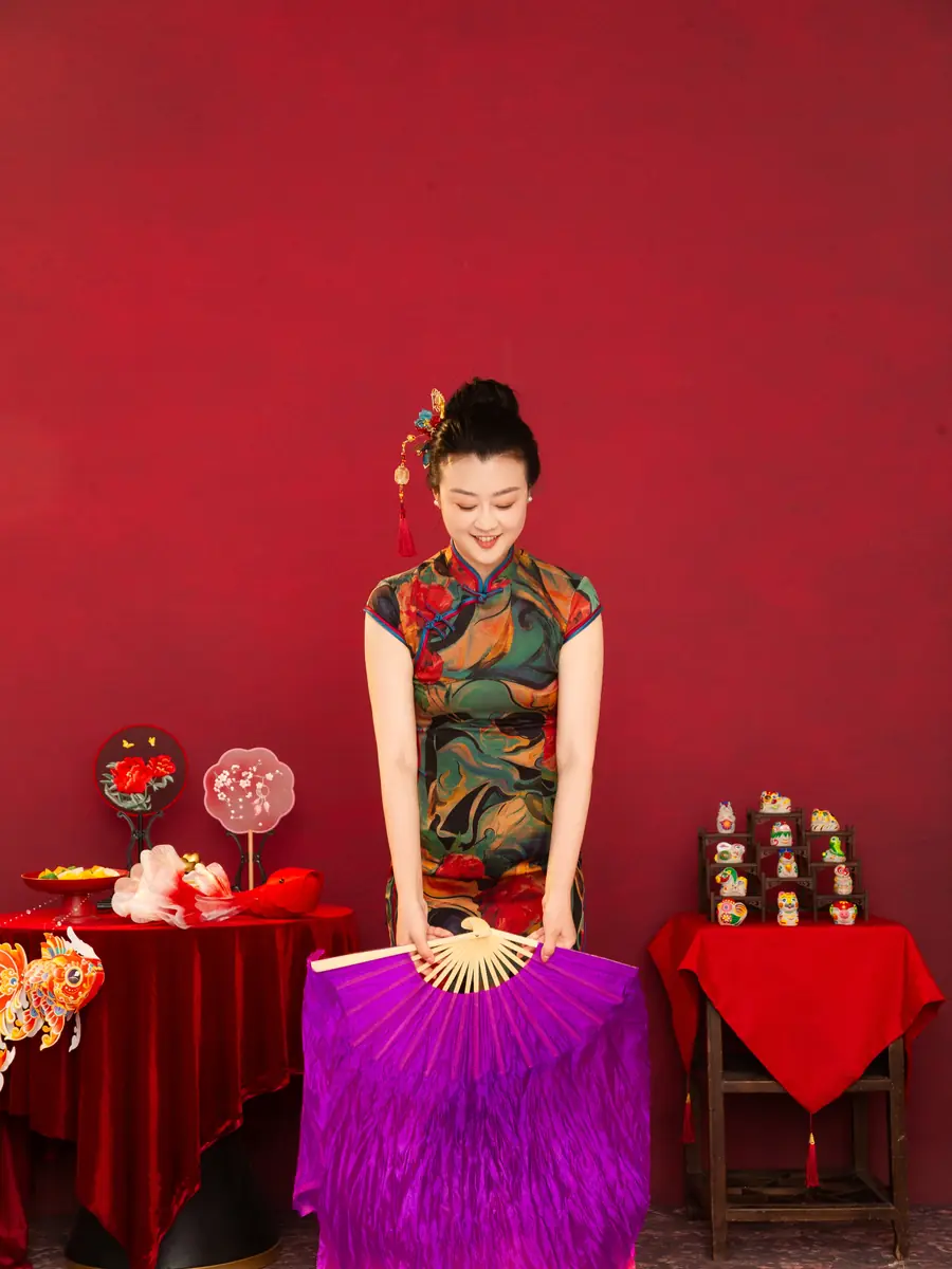 Raina in a floral qipao holding a purple silk fan